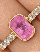 Close-up of ring on finger showing bezel-set pink sapphire and diamond accents