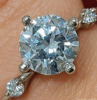 Ring on finger showing round brilliant center stone in six-prong setting