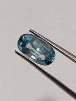 Front view of oval blue zircon held by tweezers