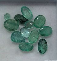 Emerald gemstones on white background showing variety of cuts and color