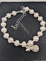 White freshwater pearl bracelet laid flat showing full strand, clasp, extender chain and pineapple charm