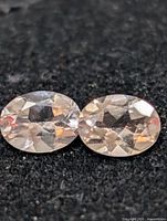 Close-up of two oval faceted pale peach gemstones on black background