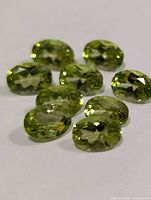 Eight oval-faceted peridot gemstones on plain background