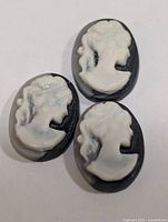 Three oval shell cameos with white female profile on dark background