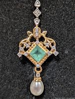 Front view of pendant showing emerald, pearl drop, and metal details