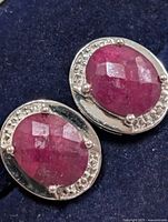 Front view of both oval ruby earrings in silver setting with clear stone accents