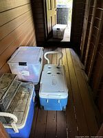 Blue wheeled Coleman cooler, plastic storage tote, additional cooler partially visible