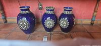 Front view of all three cobalt blue vases showing metal medallions and rim accents