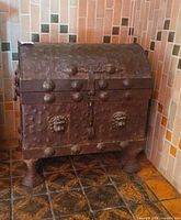 Front angled view of hammered tin trunk showing riveted surface, lion head appliqués, hasp, domed lid, and decorative feet