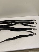 Four black belts/straps laid out showing full length and hardware