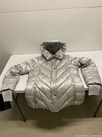 Full view of metallic silver quilted puffer jacket laid flat on table