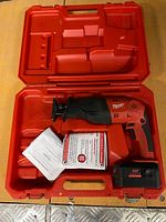 Open red Milwaukee case showing saw, battery and manuals