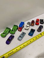 Ten assorted die-cast vehicles lined beside measuring tape