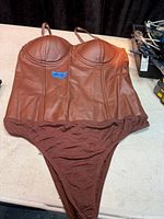 Front view of brown faux leather corset bodysuit on table