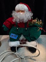 Front view of plug-in mechanical Santa atop chimney base with power cord and wreath visible