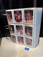 Front view of binder showing plastic pages with cards including Moses Malone, Sidney Moncrief, others