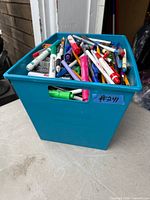 Blue bin full of assorted pens, markers, pencils