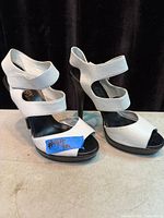 Pair of white strappy high heel shoes side view.