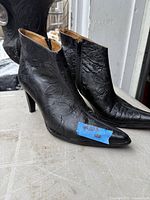 Full view of both black embossed leather ankle boots showing uppers, side zipper, pointed toes, stiletto heels