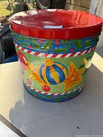 Front view of large cylindrical tin showing holiday design and red lid