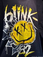 Front view of black Blink-182 T-shirt showing yellow smiley and white graphics