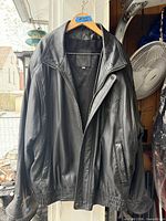 Front view of black leather jacket on hanger showing zipper, pockets, collar, lining and size tag