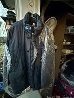Full view of dark padded winter coat on hanger with plastic cover