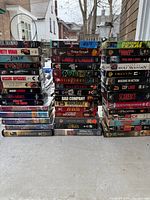 Three tall stacks of assorted VHS tapes on outdoor ledge