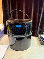 Front view of black vinyl cylindrical hat box showing handle, zipper, and surface wear