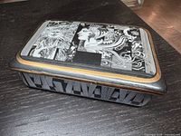 Angled view of closed porcelain trinket box showing lid artwork, gold border and side stripe pattern