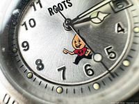 Close-up of dial showing Roots logo, numerals, hands, mascot graphic