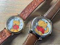 Two Timex Winnie the Pooh wristwatches side by side showing dial designs and leather straps