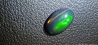 Top view of oval black opal showing bright green flash