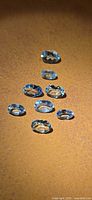 Eight light blue oval aquamarine gemstones on brown surface