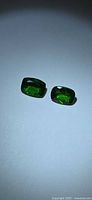 Two rectangular cushion-cut green gemstones on neutral background