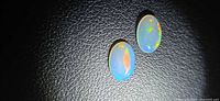 Two oval opal cabochons on black background under light showing play-of-color