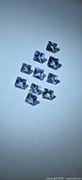 Ten square princess cut tanzanite gemstones arranged diagonally on neutral background