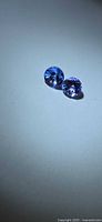 Two round blue-violet faceted gemstones on neutral background
