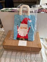Blue Christmas gift bag with Santa graphic atop cardboard box of unseen bags