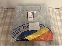 Stacked gray sweatshirt in plastic with tag and hand-written number