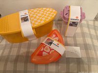 Yellow plastic oblong pasta cooker, orange egg cooker, purple rice cooker with paper sleeves