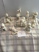 Group shot of all Snowbabies figurines and plaque on checked cloth