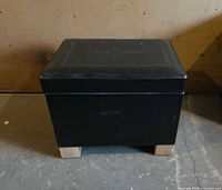 Front view of closed ottoman showing black faux leather exterior and wood legs