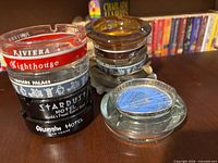 Stack of glass ashtrays with venue names, plus blue-centre ashtray beside