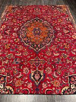 Full view of the handmade Mashhad Persian rug on dark floor