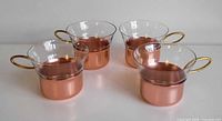 Four glass cups with copper sleeves and gold handles grouped