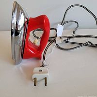 Side view of travel iron showing chrome body, red handle, cord and plug