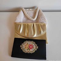Three handbags: white beaded purse, gold clutch, black floral clutch