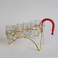 Side view of gold caddy holding six shot glasses showing red handle and glass tints
