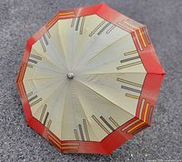 Top view of open umbrella showing cream canopy, red border, geometric stripes